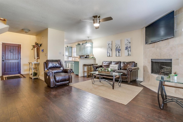 living area featuring ceiling fan, dark wood-style floors, baseboards, and a tile fireplace