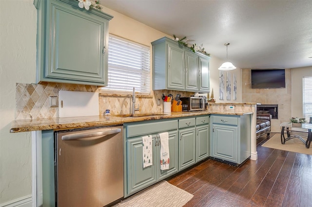 kitchen with a peninsula, a sink, dark wood-type flooring, stainless steel dishwasher, and backsplash