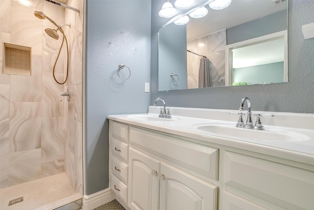 full bath with double vanity, tiled shower, visible vents, and a sink