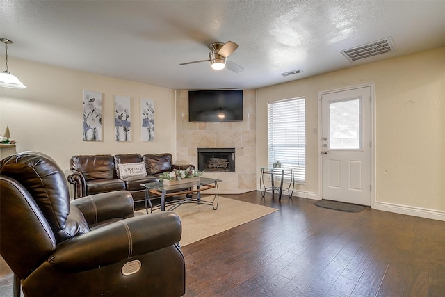 living area featuring baseboards, visible vents, dark wood-style flooring, and a tile fireplace