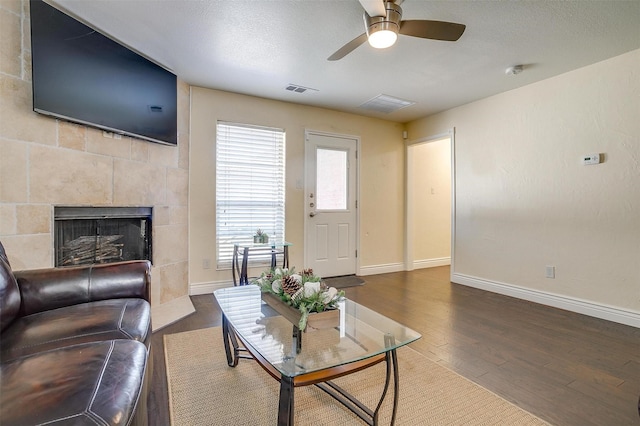 living area featuring wood finished floors, baseboards, visible vents, a tile fireplace, and a textured ceiling