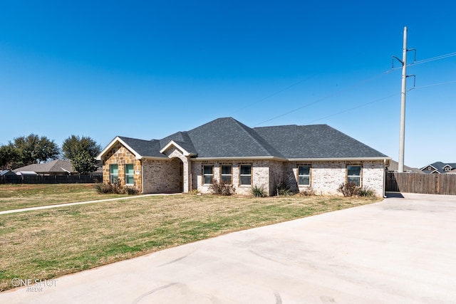 view of front of house with brick siding, a shingled roof, a front yard, and fence