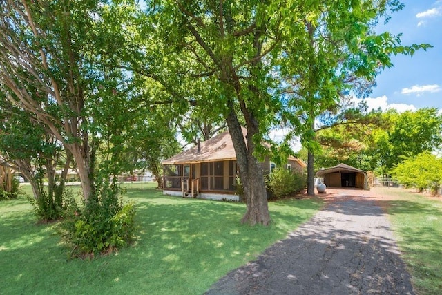 view of front facade featuring a detached carport, fence, a front yard, a sunroom, and driveway