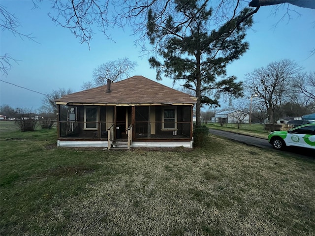 rear view of house featuring a shingled roof, a yard, and a sunroom