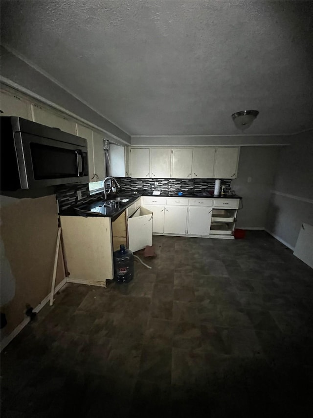 kitchen with dark countertops, a sink, white cabinetry, stainless steel microwave, and backsplash