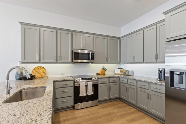 kitchen with light wood finished floors, gray cabinets, a sink, stainless steel appliances, and tasteful backsplash