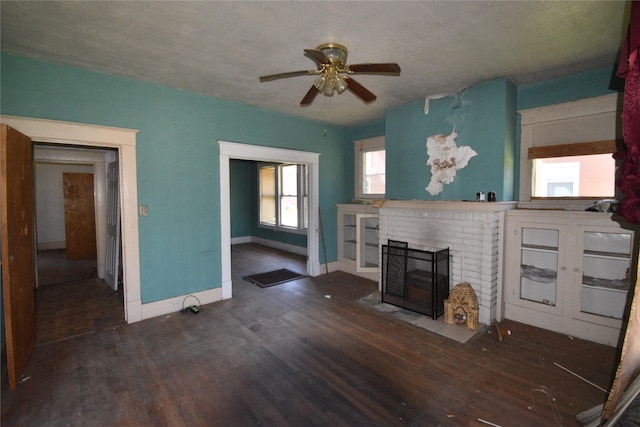 unfurnished living room with a ceiling fan, wood finished floors, baseboards, a textured ceiling, and a brick fireplace