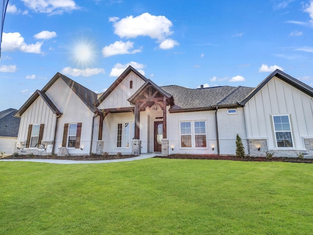 modern farmhouse with brick siding, board and batten siding, a front yard, and roof with shingles