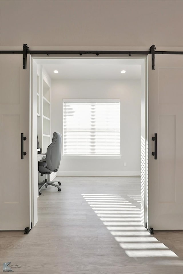 office space featuring baseboards, a barn door, and wood finished floors