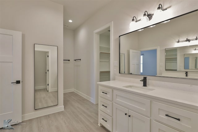 bathroom featuring a walk in closet, baseboards, recessed lighting, wood finished floors, and vanity