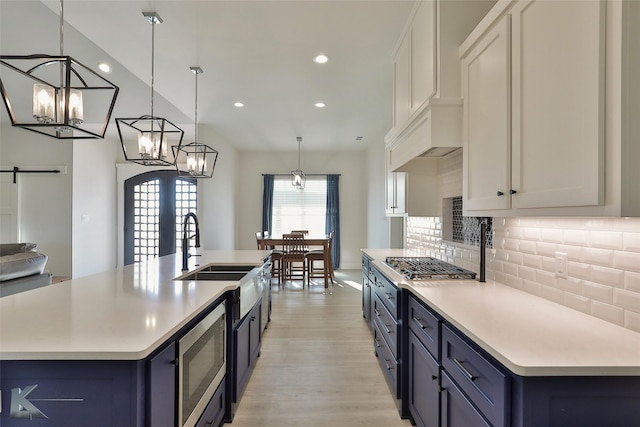 kitchen with stainless steel microwave, backsplash, blue cabinetry, light countertops, and a sink