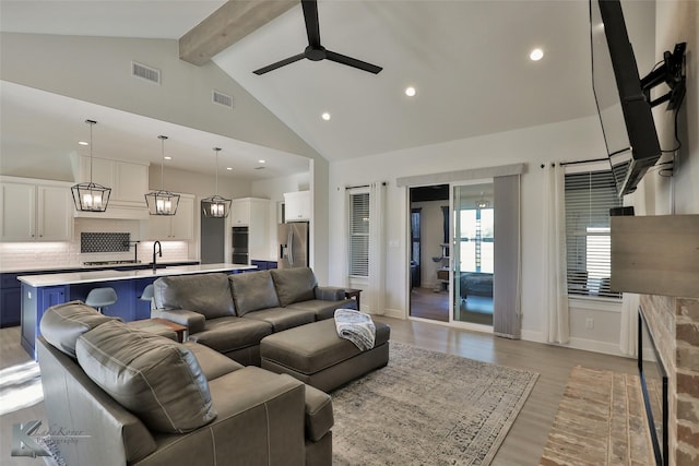 living room with visible vents, beam ceiling, high vaulted ceiling, light wood-style flooring, and a stone fireplace