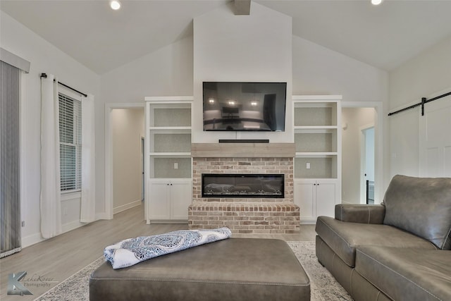 living room featuring wood finished floors, baseboards, high vaulted ceiling, a fireplace, and a barn door