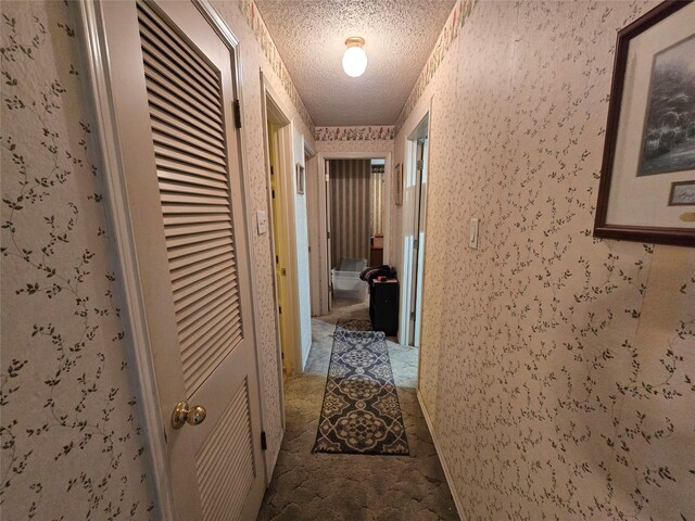 hall featuring wallpapered walls and a textured ceiling