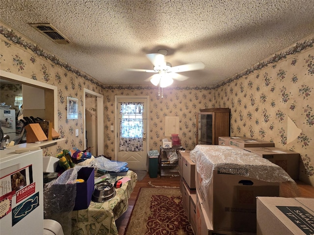 bedroom with wallpapered walls, a ceiling fan, visible vents, and a textured ceiling