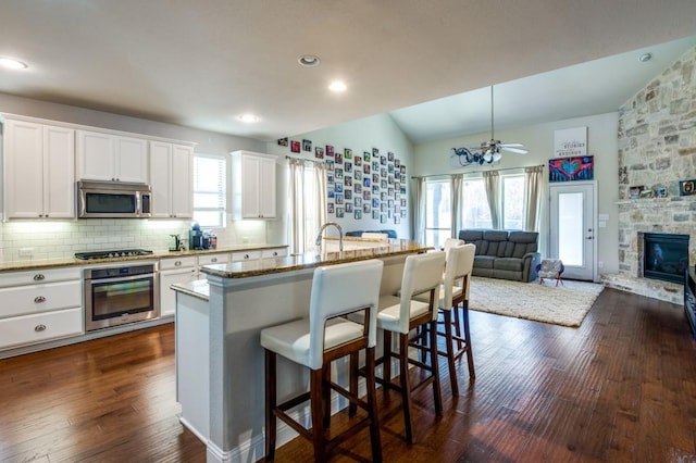 kitchen featuring dark wood-style floors, a fireplace, appliances with stainless steel finishes, a kitchen breakfast bar, and backsplash