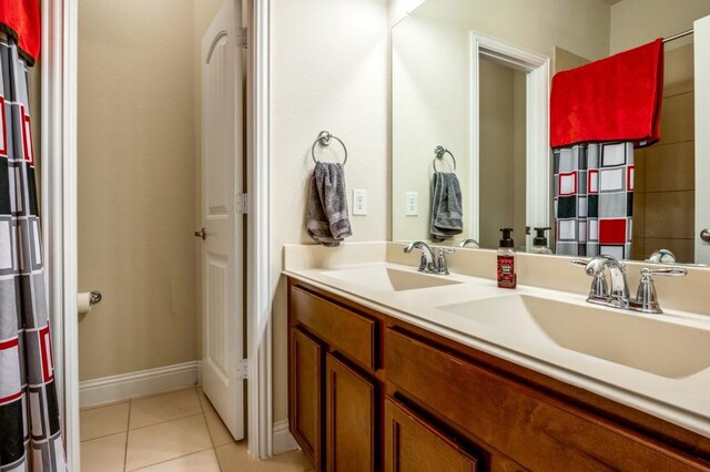 bathroom with tile patterned flooring, double vanity, baseboards, and a sink