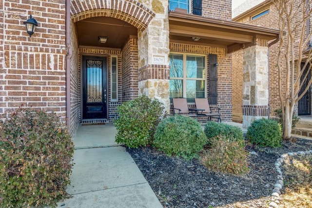 doorway to property with covered porch, brick siding, and stone siding