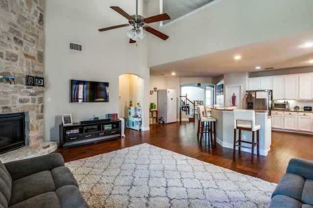 living room with arched walkways, visible vents, a stone fireplace, and dark wood-style floors