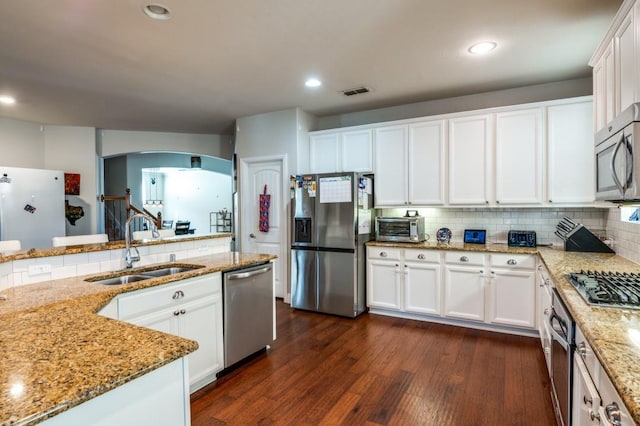 kitchen with arched walkways, a sink, stainless steel appliances, dark wood-type flooring, and backsplash