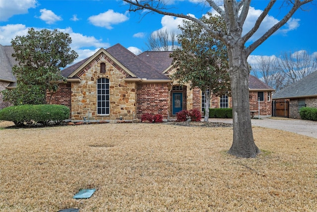 view of front facade featuring stone siding, fence, a front yard, a shingled roof, and brick siding