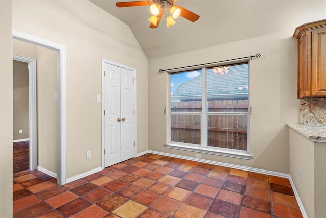 unfurnished dining area with ceiling fan, baseboards, and vaulted ceiling