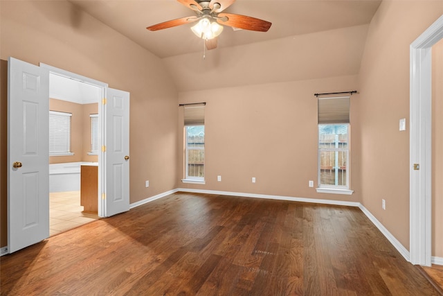 unfurnished bedroom featuring connected bathroom, baseboards, lofted ceiling, and wood finished floors