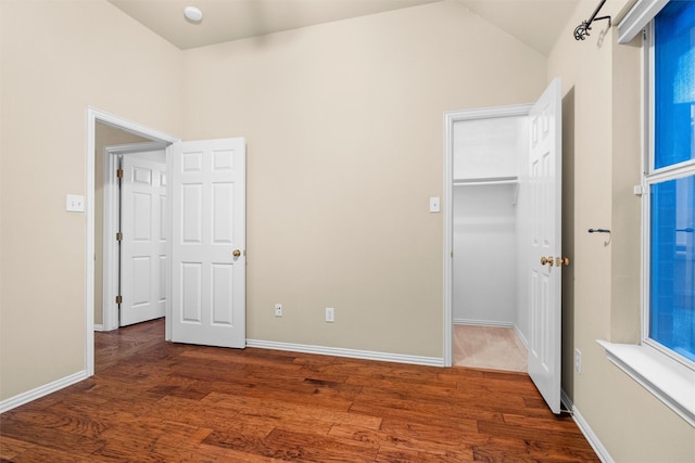 unfurnished bedroom featuring vaulted ceiling, a walk in closet, baseboards, and wood finished floors