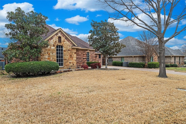 view of front of property featuring a front lawn, central AC unit, stone siding, and a shingled roof