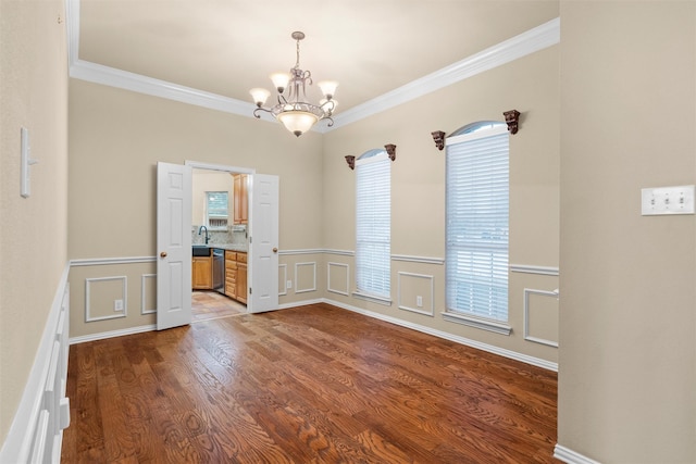 unfurnished room featuring a chandelier, ornamental molding, wainscoting, wood finished floors, and a decorative wall