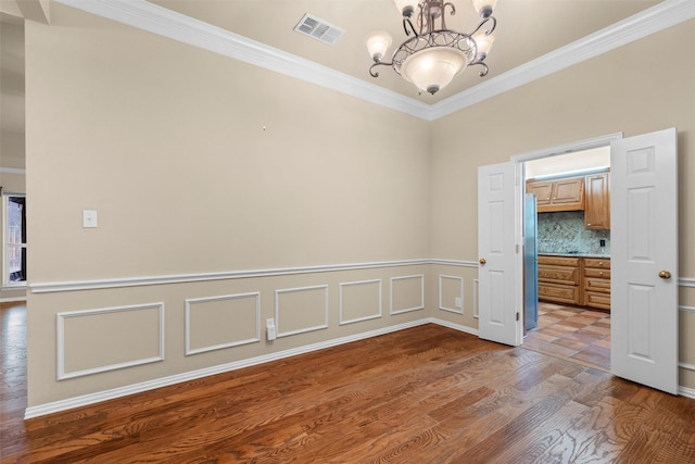 unfurnished room featuring a notable chandelier, wood finished floors, visible vents, and ornamental molding