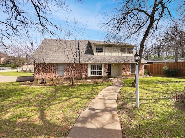 view of front of home featuring a front lawn, fence, brick siding, and roof with shingles