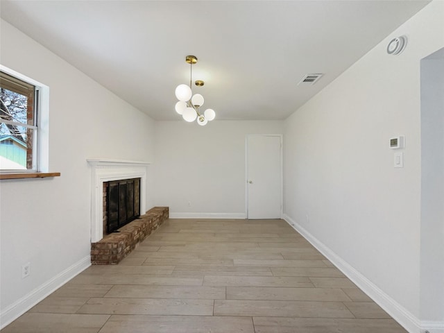 unfurnished living room featuring visible vents, a brick fireplace, baseboards, light wood-style floors, and a notable chandelier