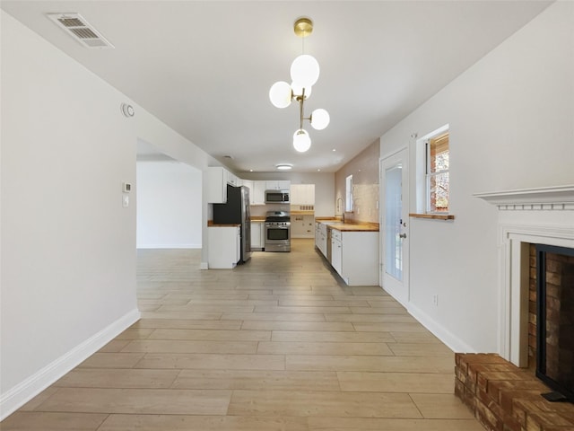 kitchen with visible vents, a fireplace with raised hearth, appliances with stainless steel finishes, white cabinetry, and a sink