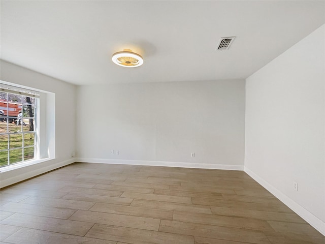 empty room featuring visible vents, light wood-type flooring, and baseboards