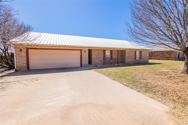 ranch-style home featuring a front yard, concrete driveway, a garage, brick siding, and metal roof