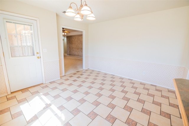 spare room featuring a wainscoted wall, ceiling fan with notable chandelier, and wallpapered walls