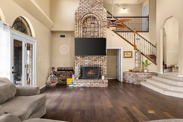 living area featuring a brick fireplace, a high ceiling, a ceiling fan, and hardwood / wood-style flooring