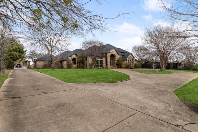 french country inspired facade featuring a chimney, concrete driveway, a front lawn, stone siding, and brick siding