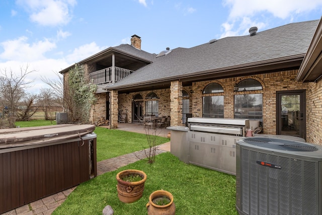 exterior space featuring a lawn, a balcony, a shingled roof, brick siding, and central AC unit