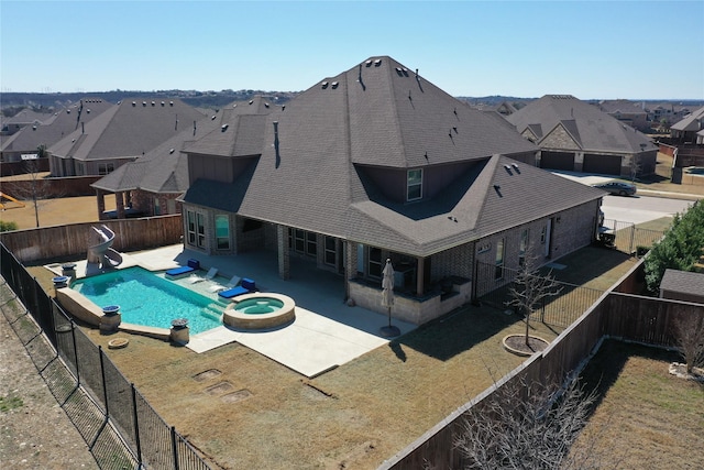 view of swimming pool with a patio, a pool with connected hot tub, a water slide, and a fenced backyard