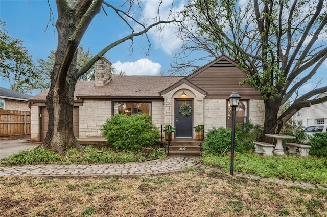 view of front of house featuring a shingled roof, fence, stone siding, and a chimney