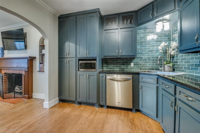 kitchen featuring tasteful backsplash, light wood-type flooring, appliances with stainless steel finishes, a fireplace, and a sink