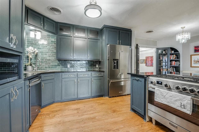 kitchen featuring visible vents, a sink, appliances with stainless steel finishes, dark countertops, and light wood-type flooring