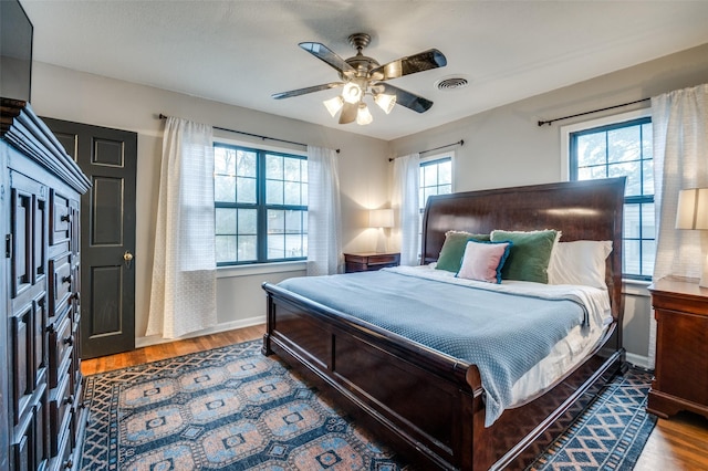 bedroom featuring visible vents, baseboards, wood finished floors, and a ceiling fan