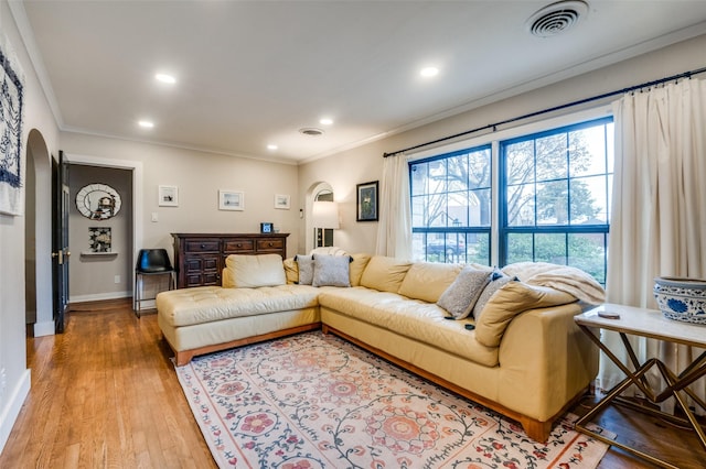 living room featuring visible vents, light wood-style flooring, ornamental molding, recessed lighting, and arched walkways