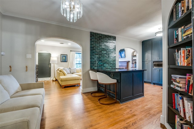 interior space with light wood finished floors, dark countertops, open floor plan, a breakfast bar, and arched walkways