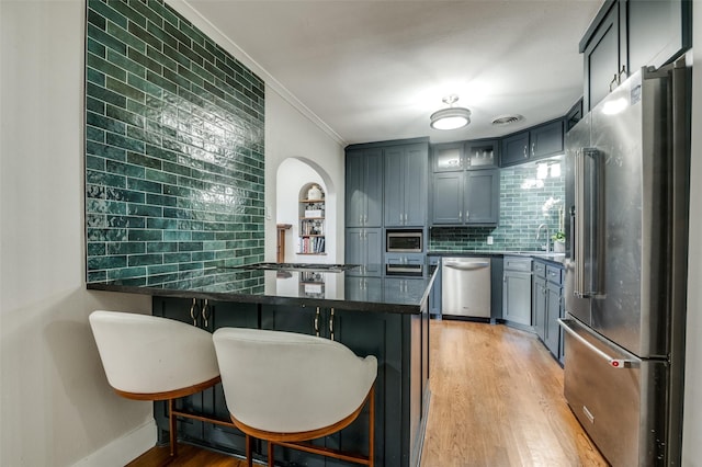 kitchen with backsplash, light wood-style flooring, a kitchen breakfast bar, appliances with stainless steel finishes, and a peninsula