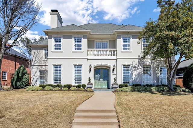 view of front of property with a shingled roof, a front yard, stucco siding, french doors, and a chimney