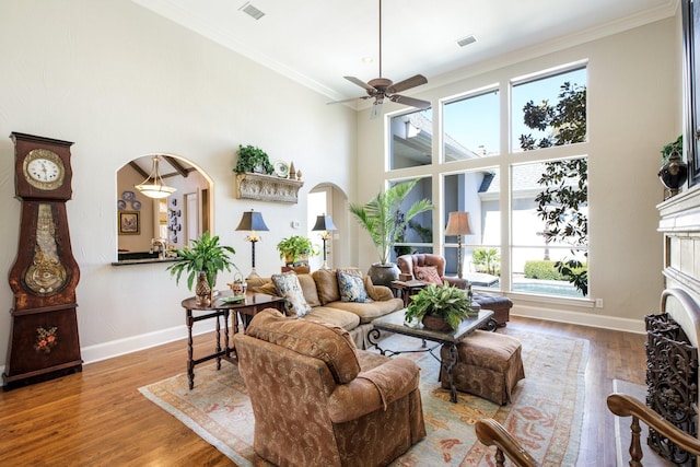 living area with arched walkways, visible vents, wood finished floors, and ornamental molding